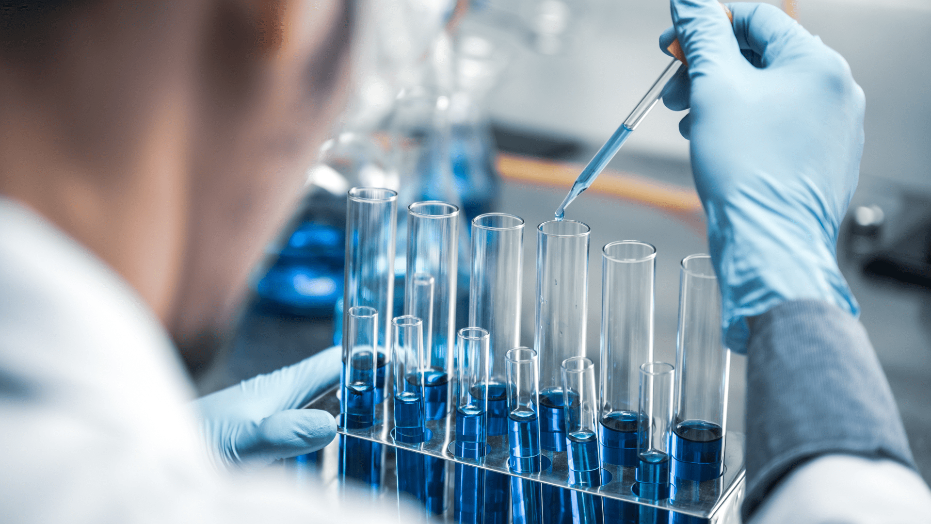 A close-up of a scientist in a lab using a pipette to add a blue liquid to a row of test tubes